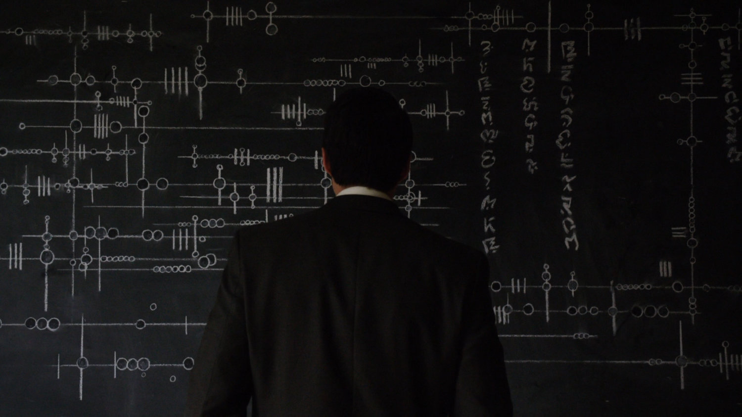 Ward in front of chalkboard with strange alien writing on it.
