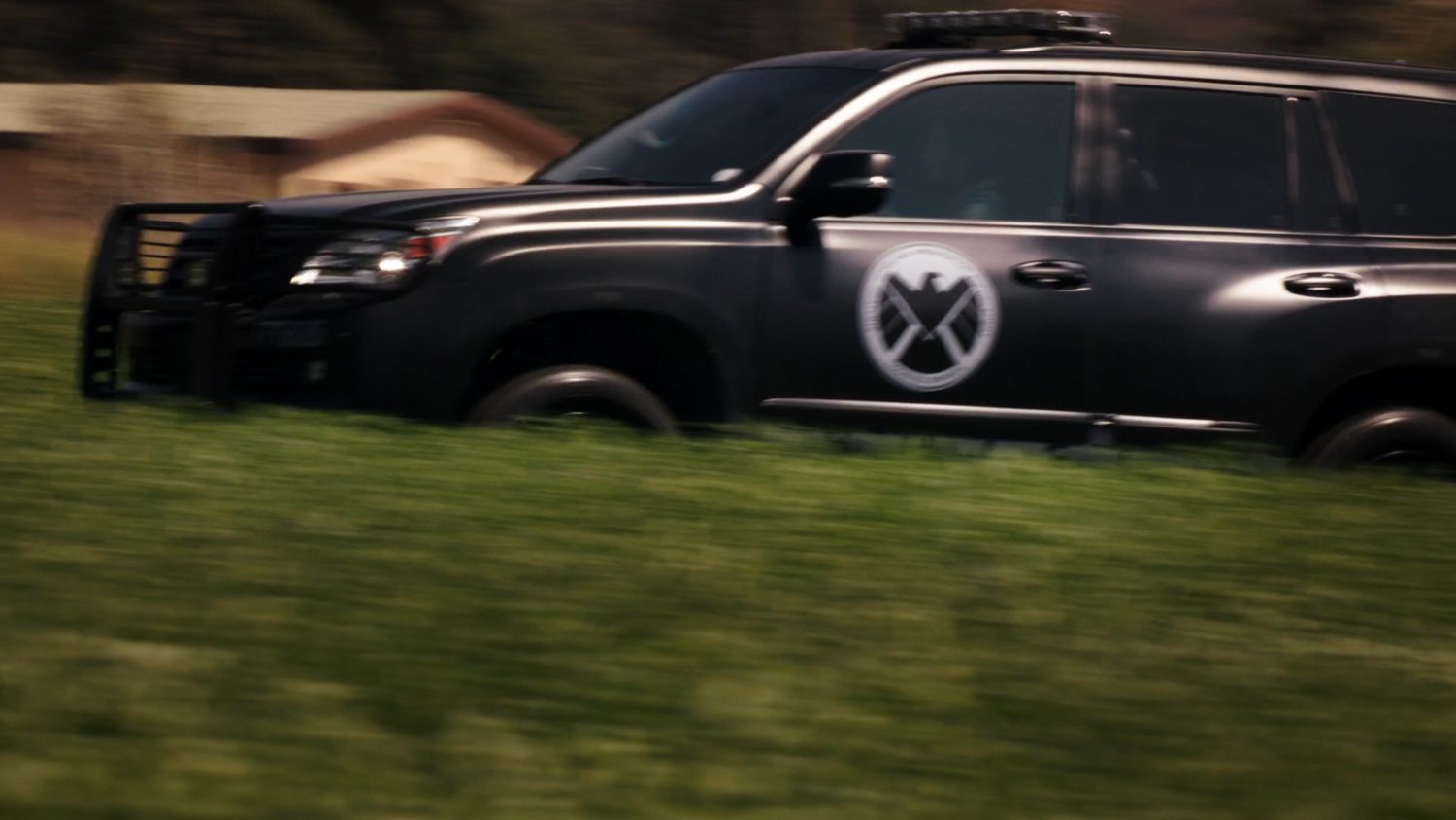 A SHIELD SUV drives through a small field.