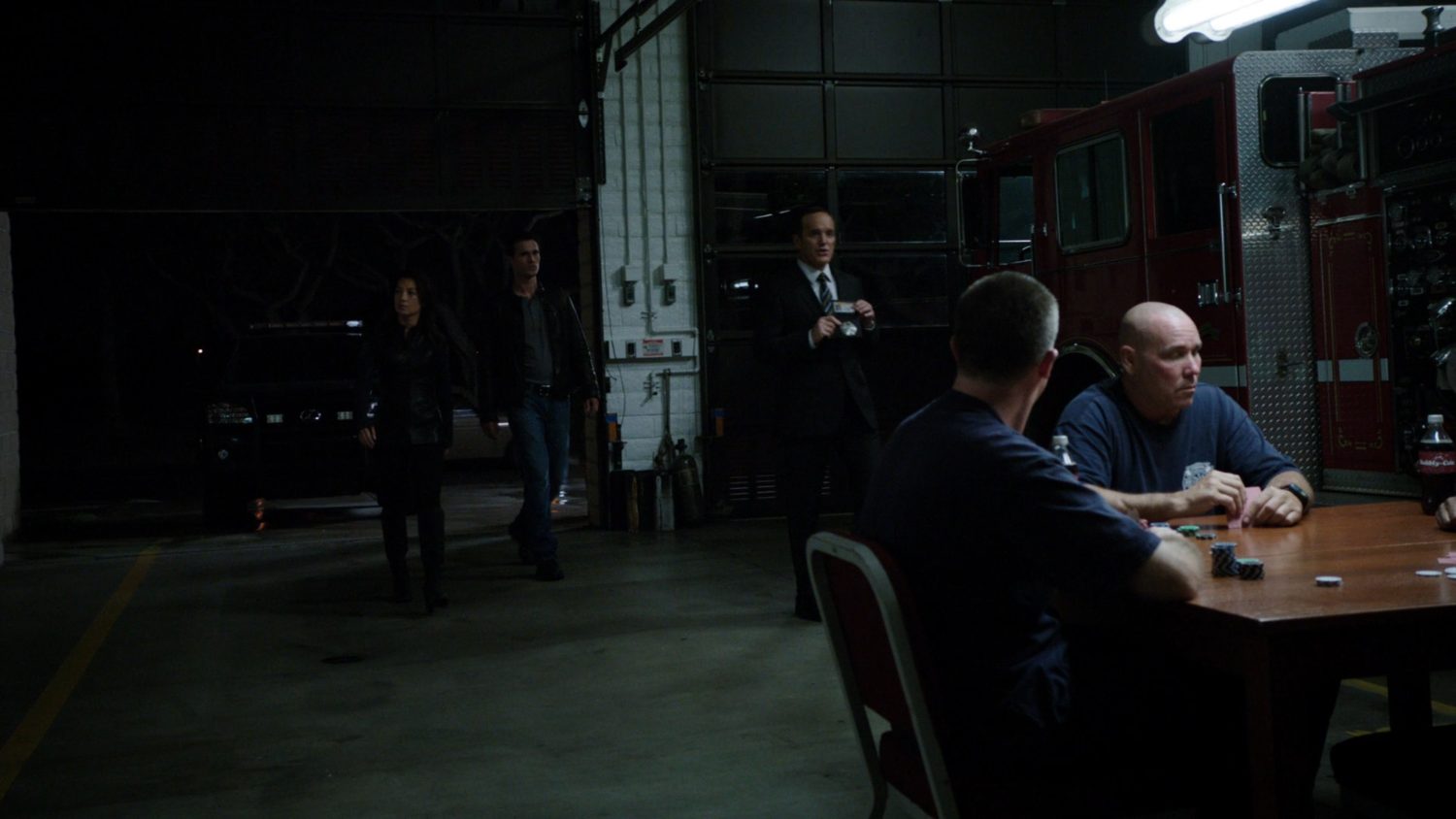SHIELD Agents enter Fire Station 77 at night, as firefighters play cards at table.