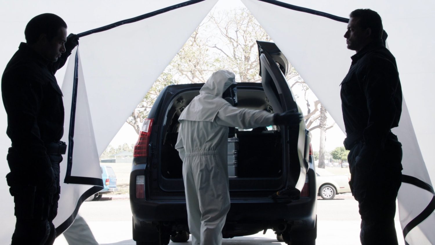 A SHIELD tech in hazmat gear loads a box into an SUV at Station 77.