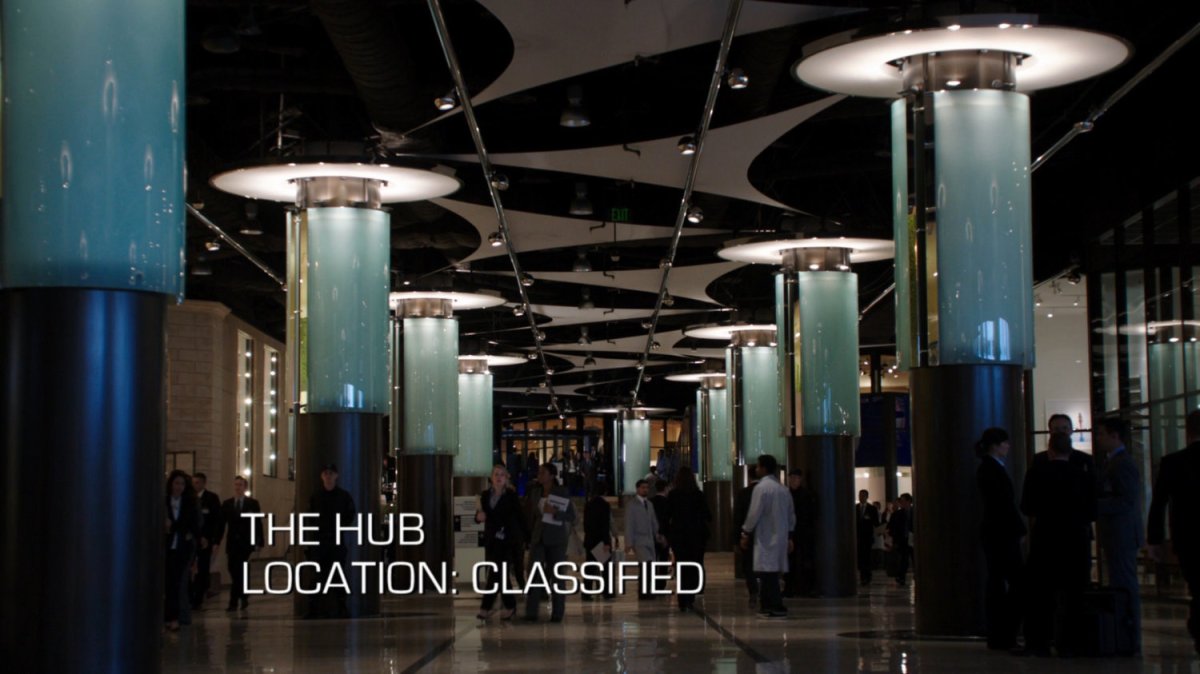 Interior hallway of The Hub with lit, glass columns. Text: The Hub, Location: Classified.