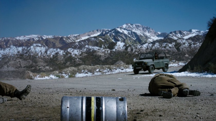 A Jeep approaches two prone guards at a Caucasus Mountain open area.