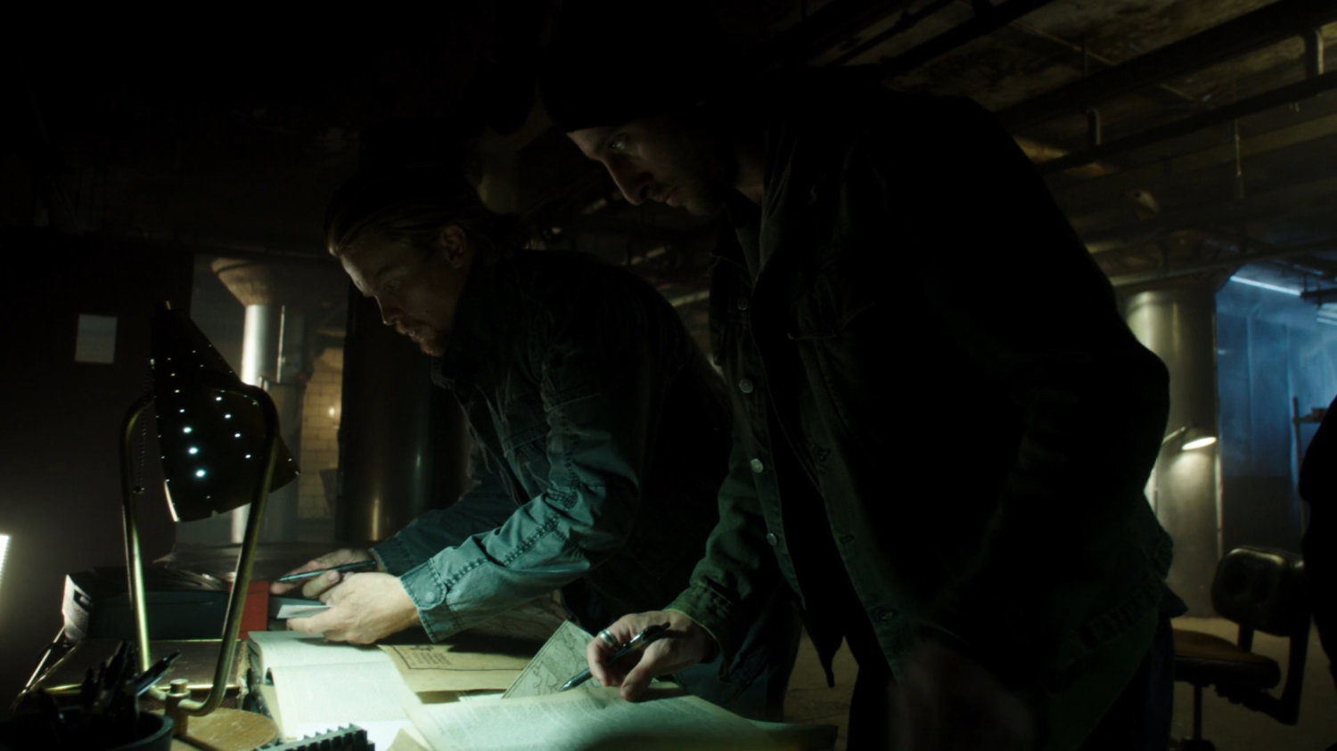 Jakob in a dark underground fight club looking over a staff and maps.