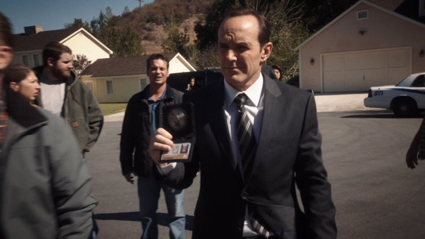 Coulson shows his SHIELD badge to onlookers in a cul-de-sac.