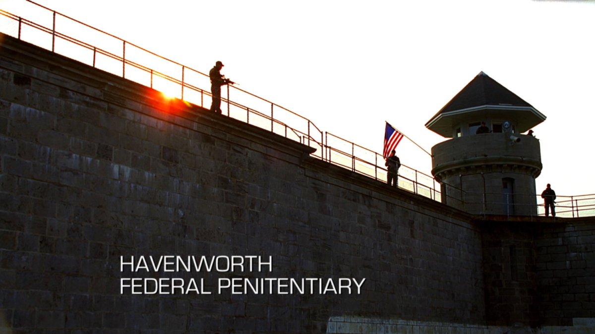 Armed guards on tall brick wall with American flag. Text: Havenworth Federal Penitentiary.