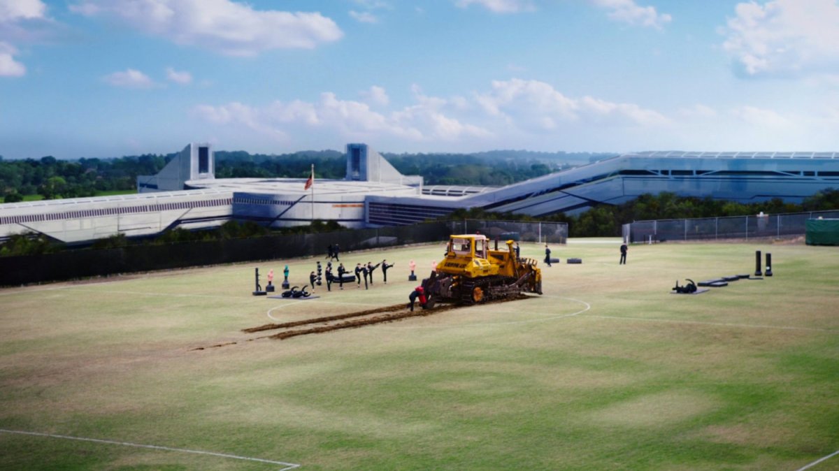 Wide shot of SHIELD athletic field with Mike Peterson pushing giant bulldozer.