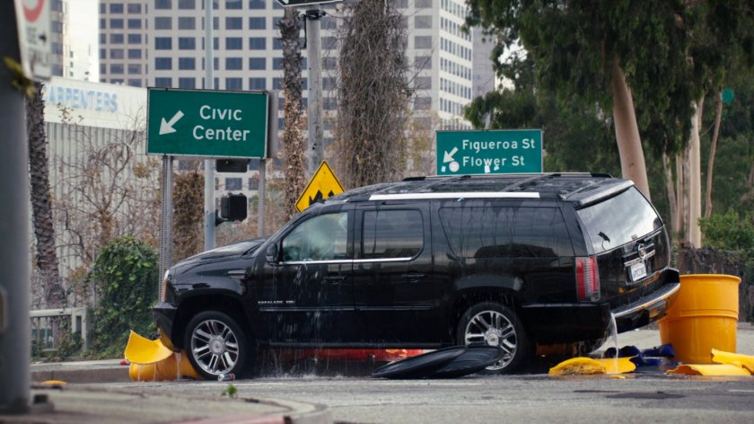 Wet, black SUV stopped up on curb in Los Angeles intersection.