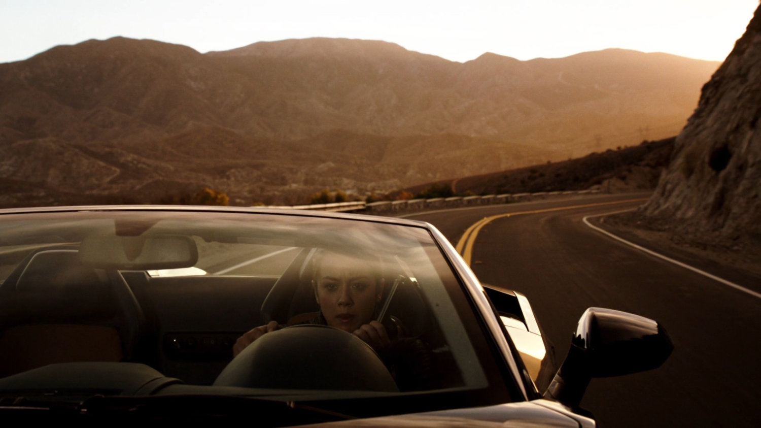 Skye in a sports car on a mountainous road.