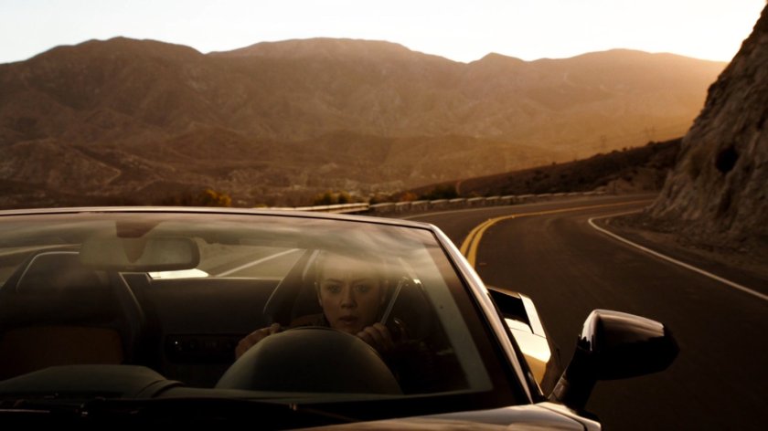 Skye in a sports car on a mountainous road.