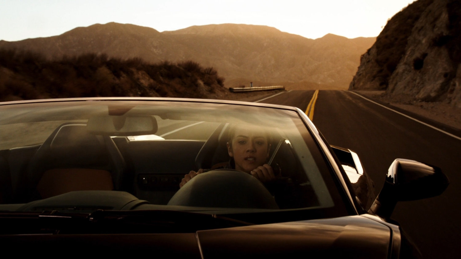 Skye in a sports car on a mountainous road.
