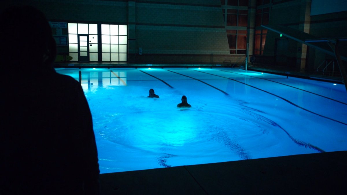 Two people swim in an interior pool at night.