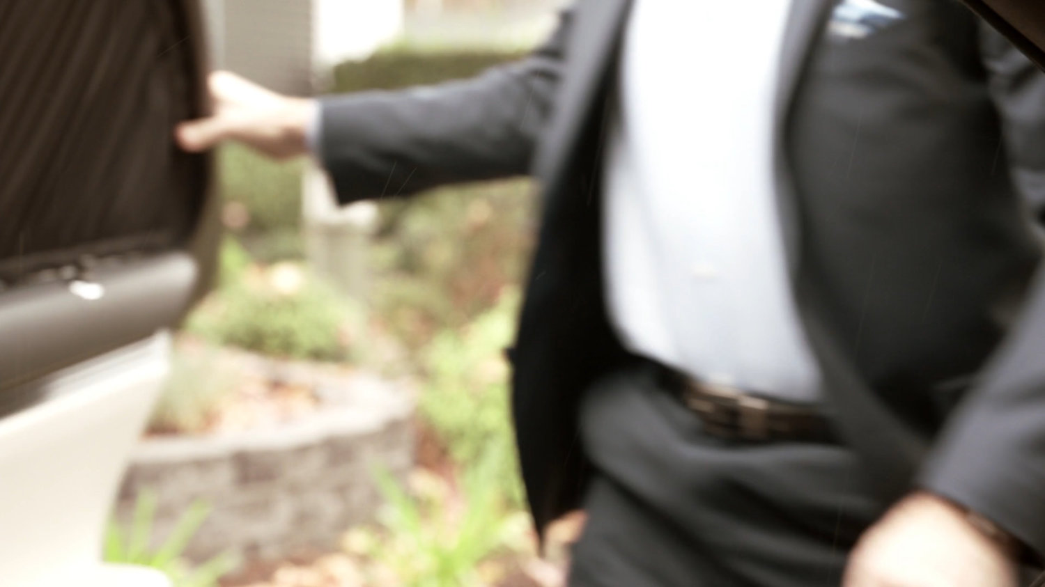 Blurry vegetation outside car door as Ian Quinn exits car.