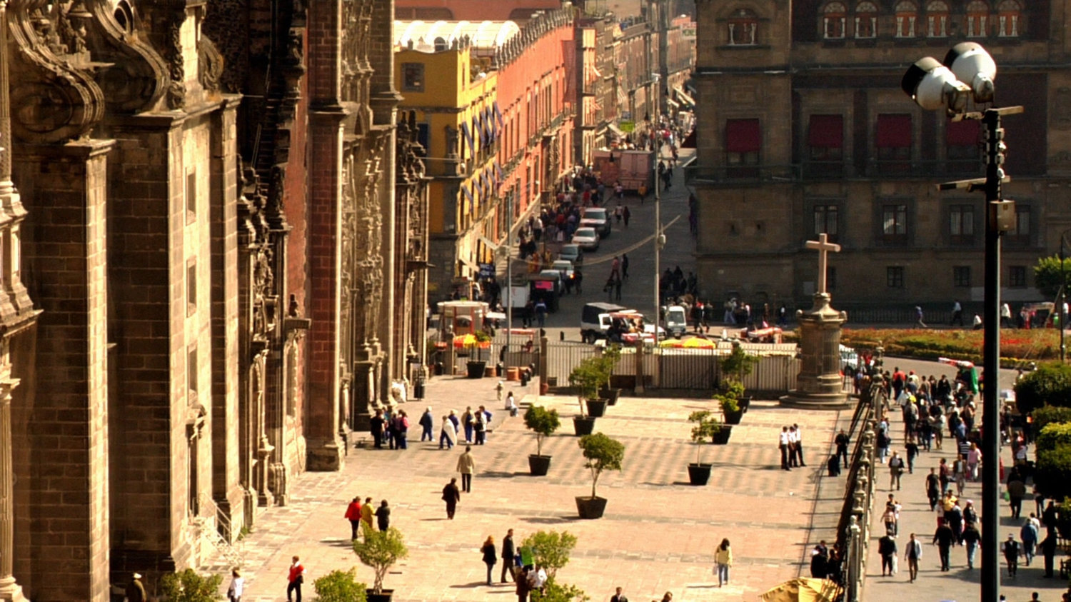 Long shot of Mexico City plaza with pedestrians and cars, next to church.