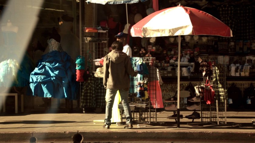 Sidewalk racks of clothes for sale by large umbrella.