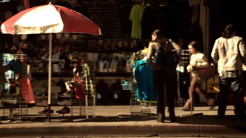 Sidewalk racks of clothes for sale by large umbrella.