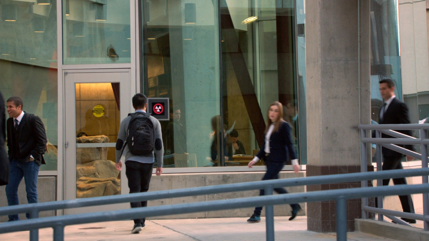 Ward and Simmons walking through SHIELD academy walkway by large window.
