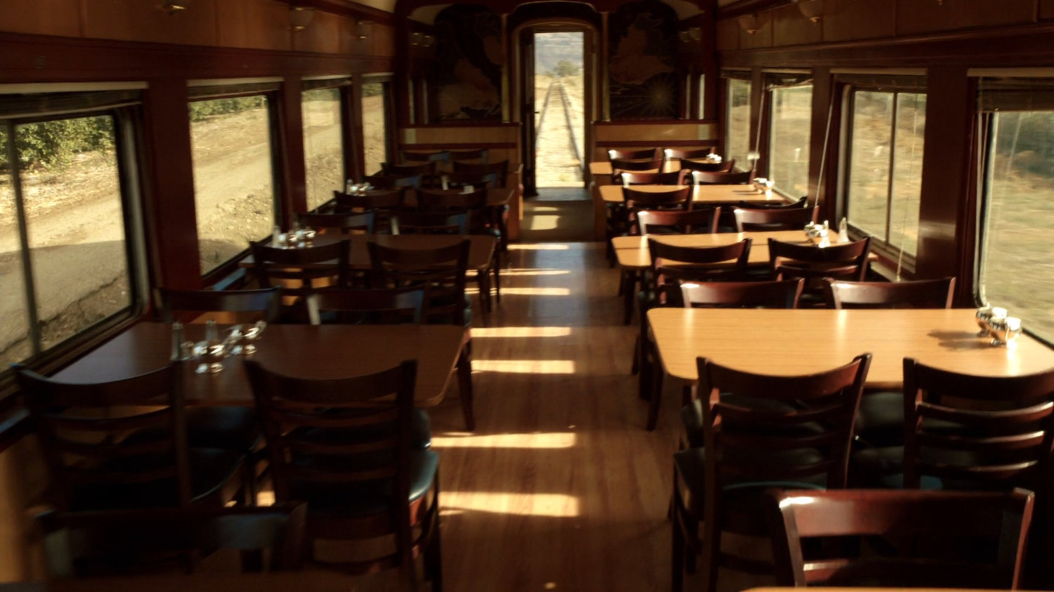 An empty dining car and the surrounding exterior of the train.