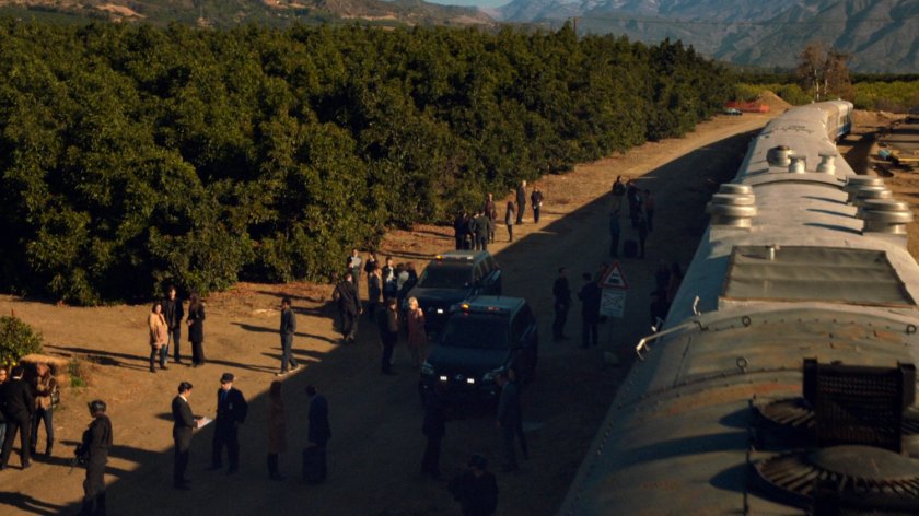 A stopped train next to a grove of trees with passengers and police milling around.