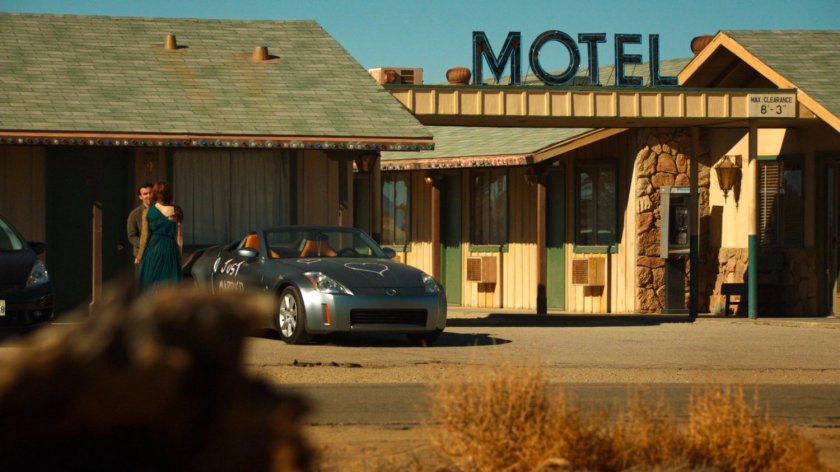 A newlywed couple by a car in front of a motel in Death Valley.