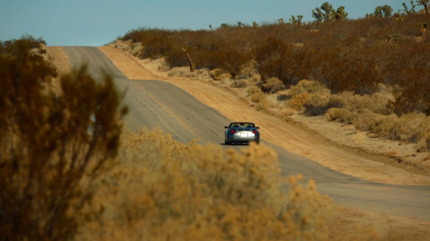 A car drives away down a hilly Death valley highway.