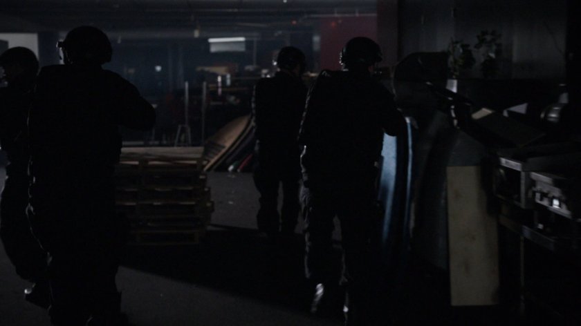 SHIELD agents advance inside a dark racetrack interior.