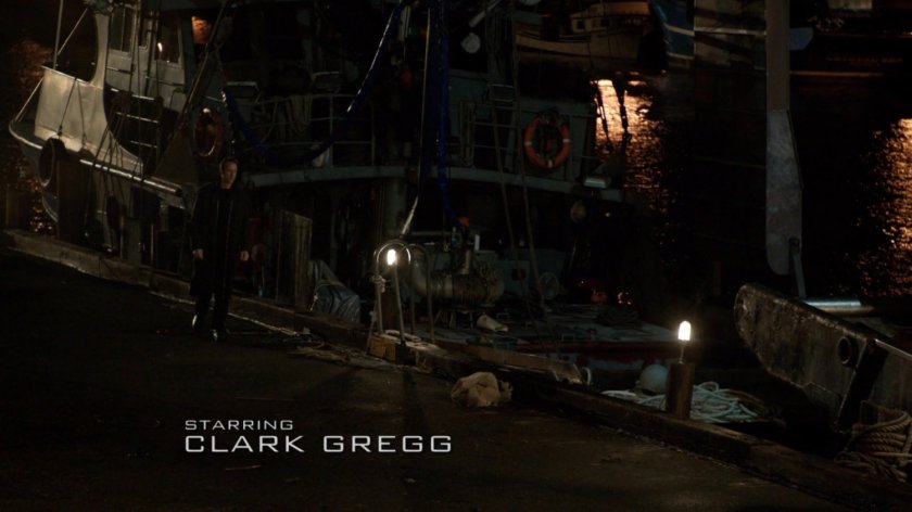 High angle nighttime view of man walking by boat docked at a pier.
