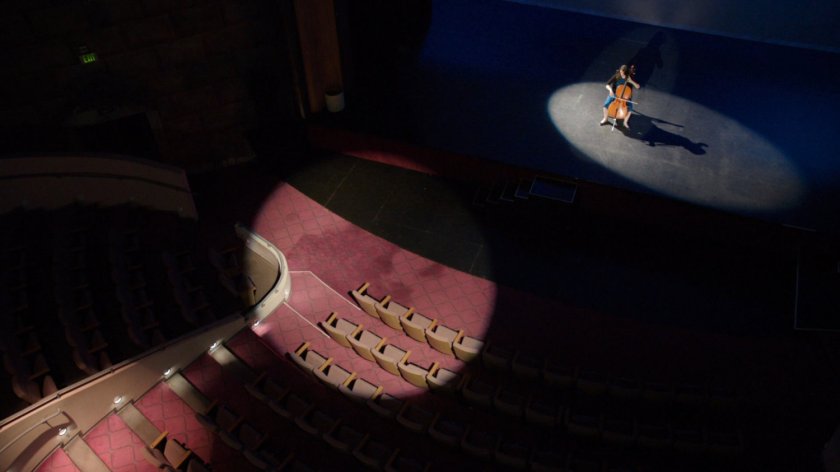 High angle of spotlit Portland theater stage, with Audrey Nathan playing cello.