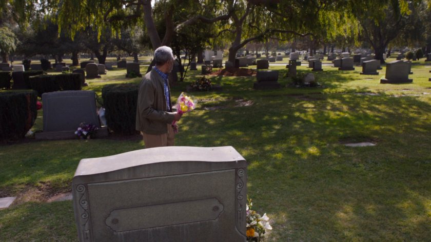 An old man in a cemetery watches someone dig up a grave.