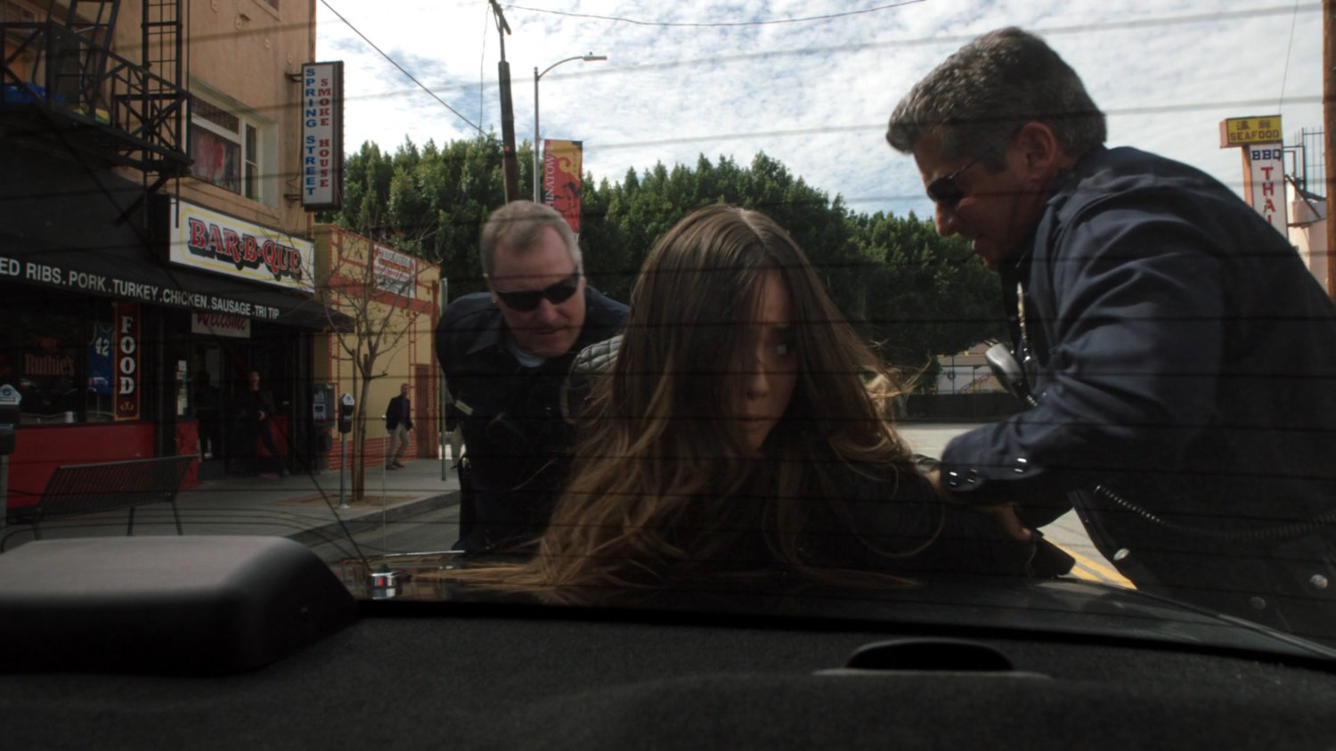 Skye is cuffed by two police officers on the trunk of their squad car.