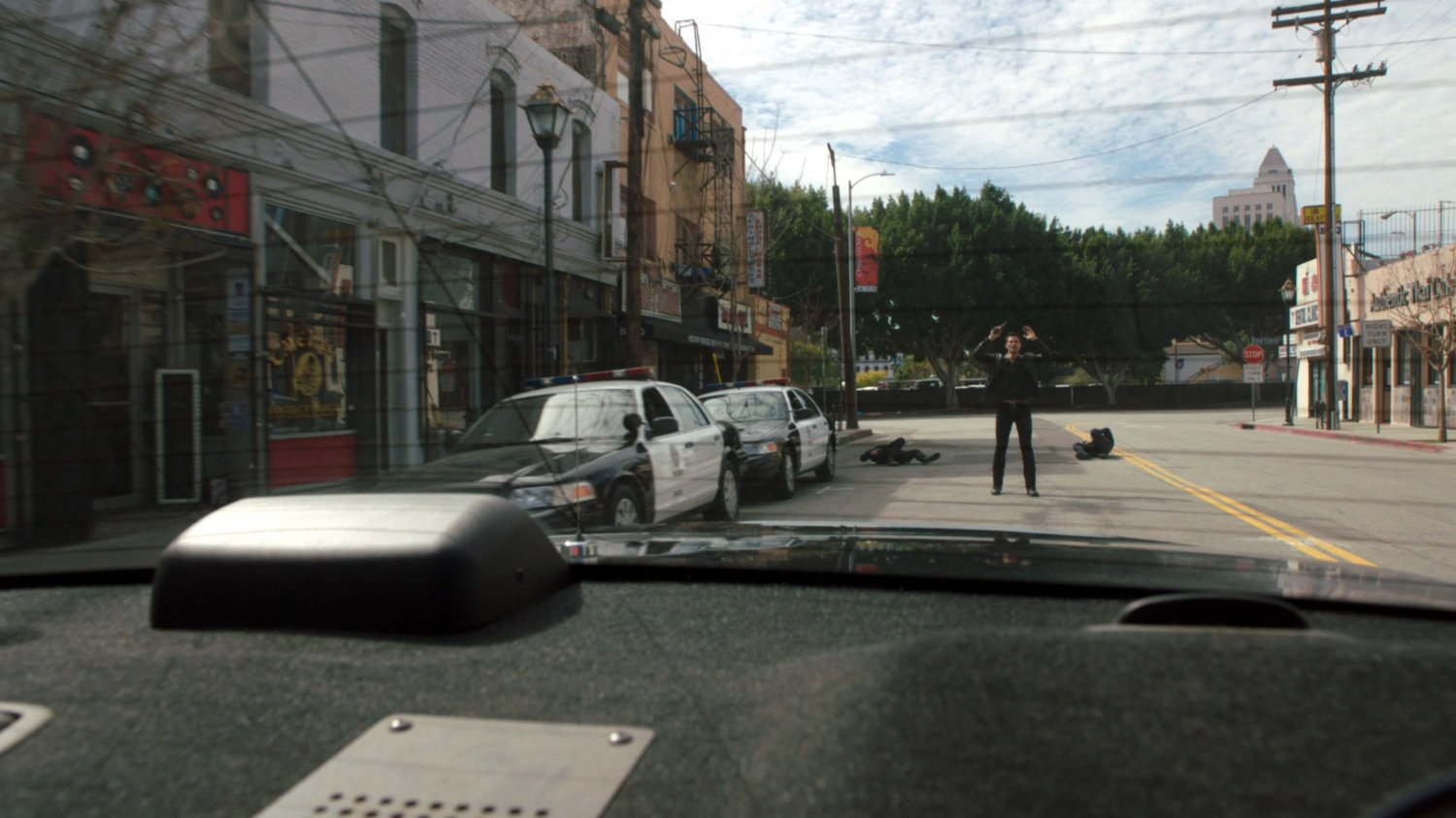 POV of Ward with hands in air from rear of police car as it drives away.