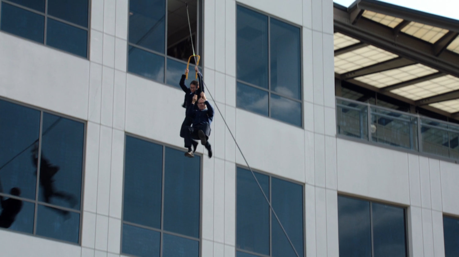 Exterior modern office building with May and Coulson sliding out on a zip line.