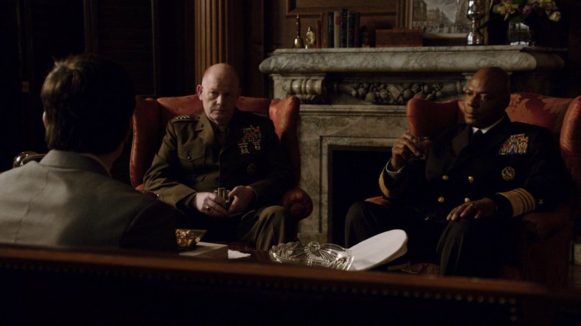 Two military advisors confer with Ian Quinn in an officer's club.