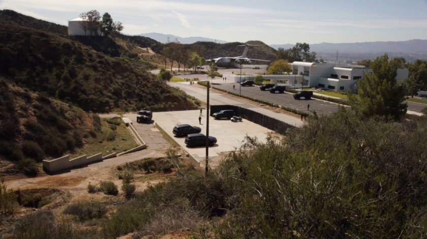 Wide shot of the Cybertek Manufacturing Facility with various vehicles, and The Bus parked nearby.