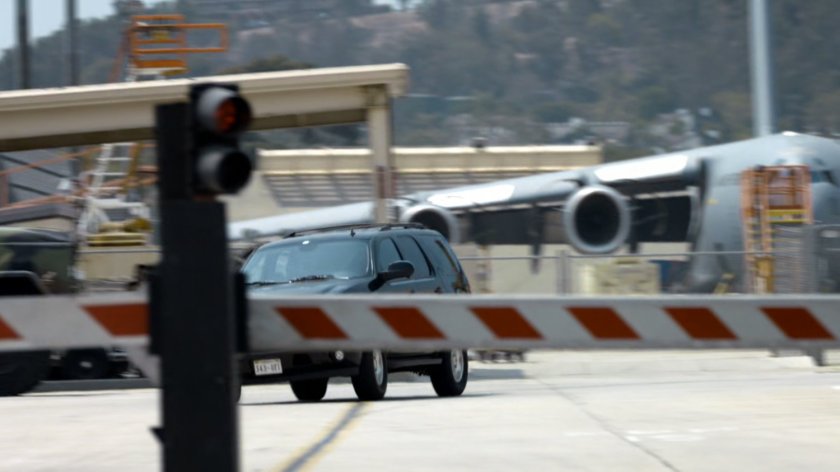 SUV racing towards security checkpoint of Marine Base, with Globemaster in background.