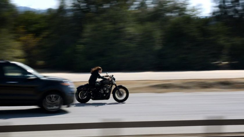 Agent May racing along a busy road on a motorcycle.