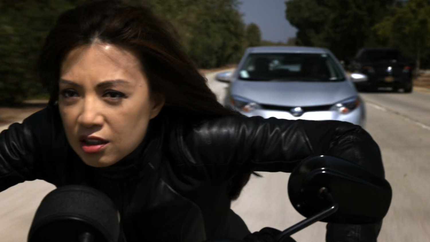 Agent May racing along a busy road on a motorcycle.