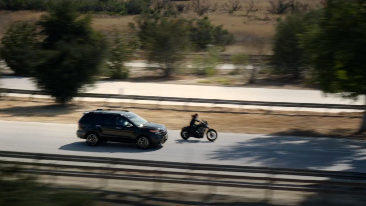 Agent May racing along a busy road on a motorcycle.