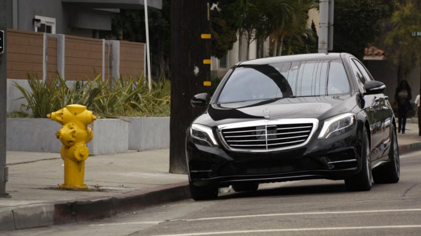 Black Mercedes pulling up to curb on street.