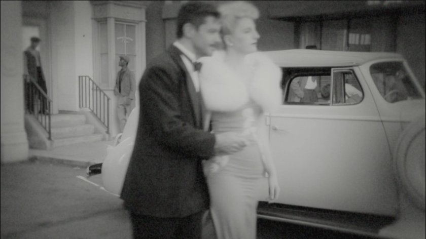 Howard Stark and woman walk past car.