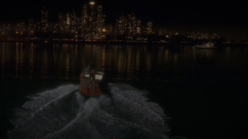 Stark drives boat away from Wharf 17 towards city at night.