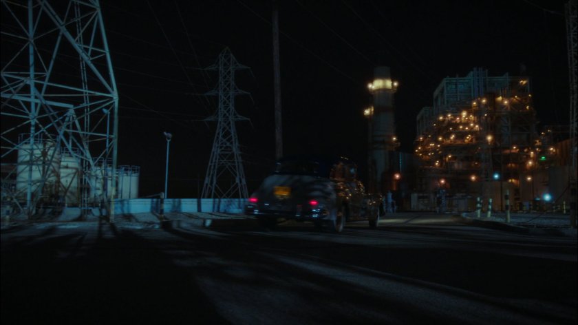 Car drives past Roxxon refinery.