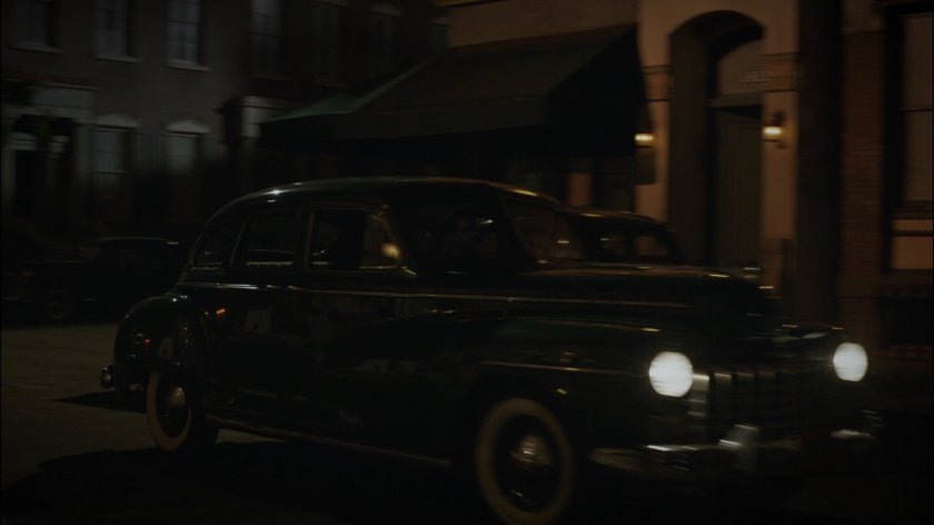 Car takes corner on dark New York city street.