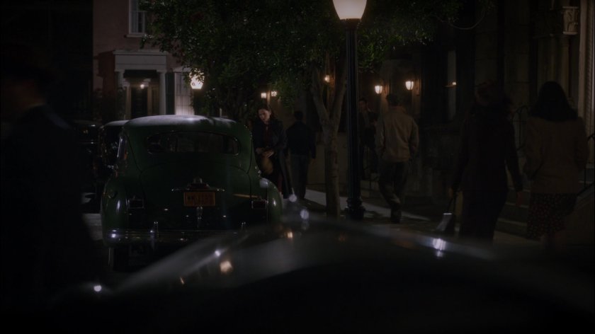 Peggy by parked car of dark city street, across from the Griffith Hotel.