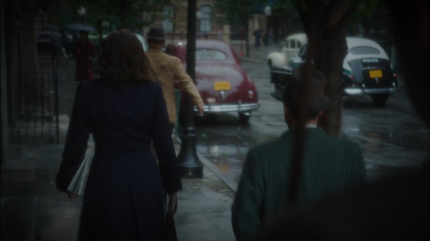 Peggy walking along a rainy New York sidewalk.