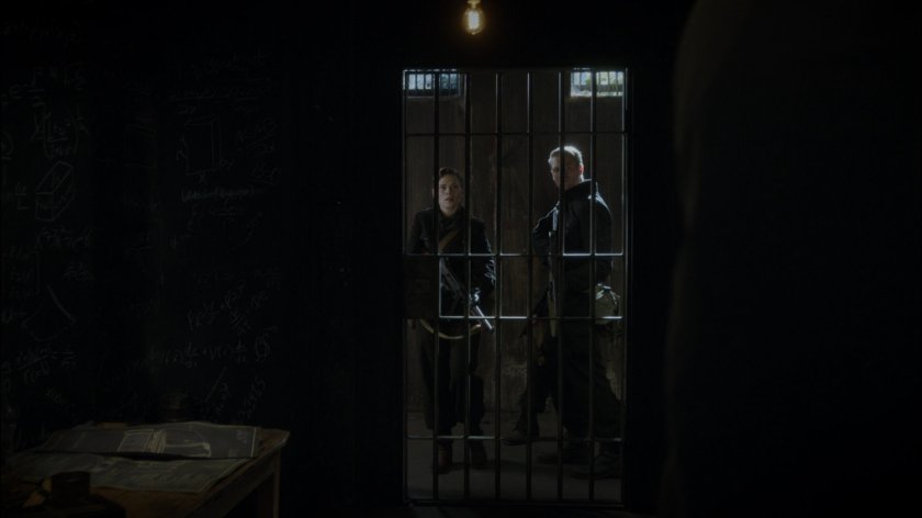 Peggy and Thompson seen through bars of prison cell.