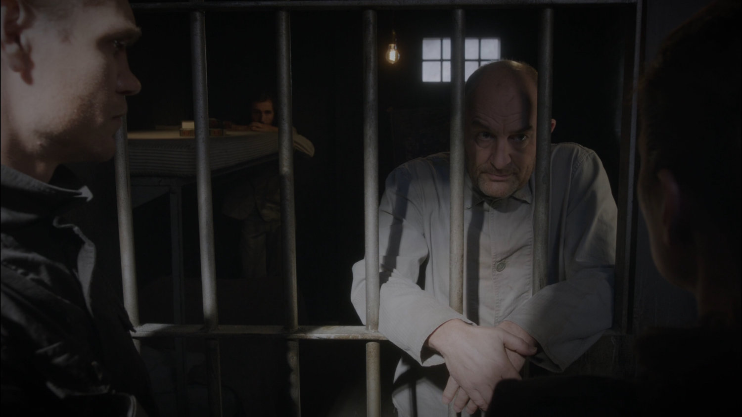 Dr. Ivchenko leans through bars of a cell.