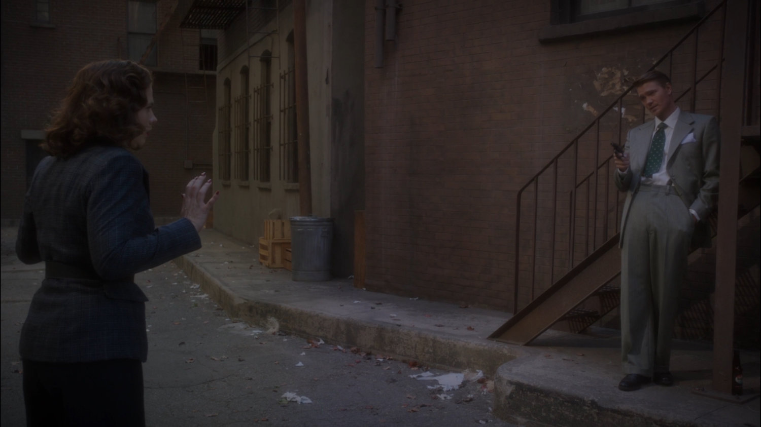 Thompson confronts Peggy in alley behind Automat.