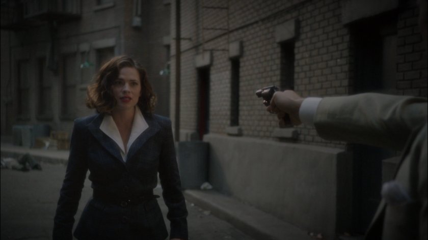Sousa holds hun on Peggy in alley behind Automat.