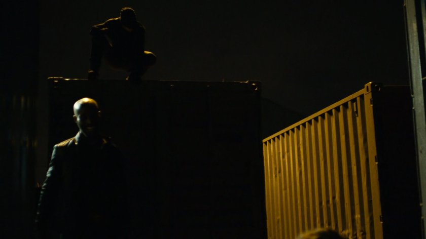 Daredevil perched above Turk at a dark container yard in Brooklyn.