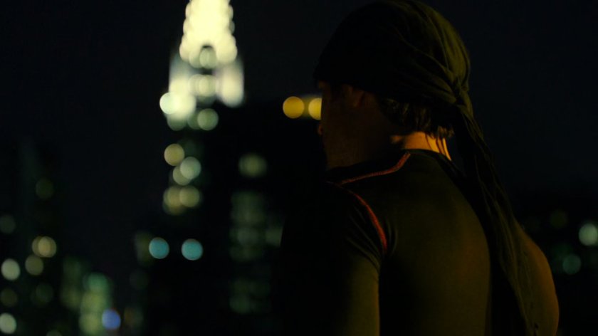 Daredevil on a rooftop listening to the city. The Chrysler building is out of focus in background.